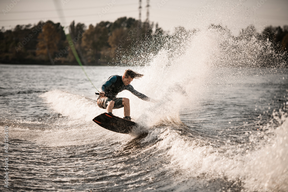 male wakeboarder in life jacket holds rope with his hands and balances on splashing wave