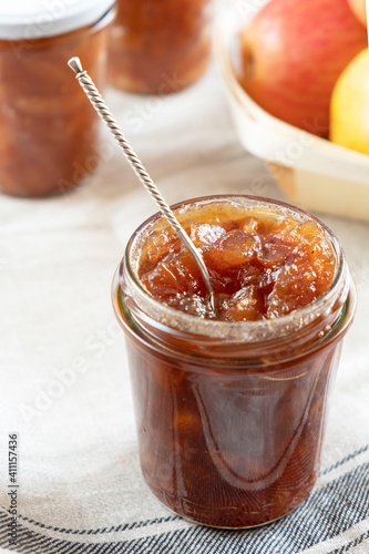 Homemade apple jam marmalade with cloves and cinnamon from organic apples in a transparent glass jar with two vintage retro spoon. Homemade autumn jam preserves.