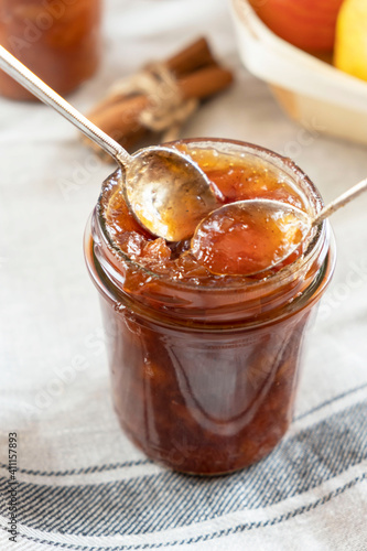 Homemade apple jam marmalade with cloves and cinnamon from organic apples in a transparent glass jar with two vintage retro spoon. Homemade autumn jam preserves.