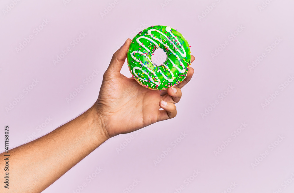 Hand of hispanic man holding donut over isolated pink background. Hand of hispanic man holding donut over isolated pink background.