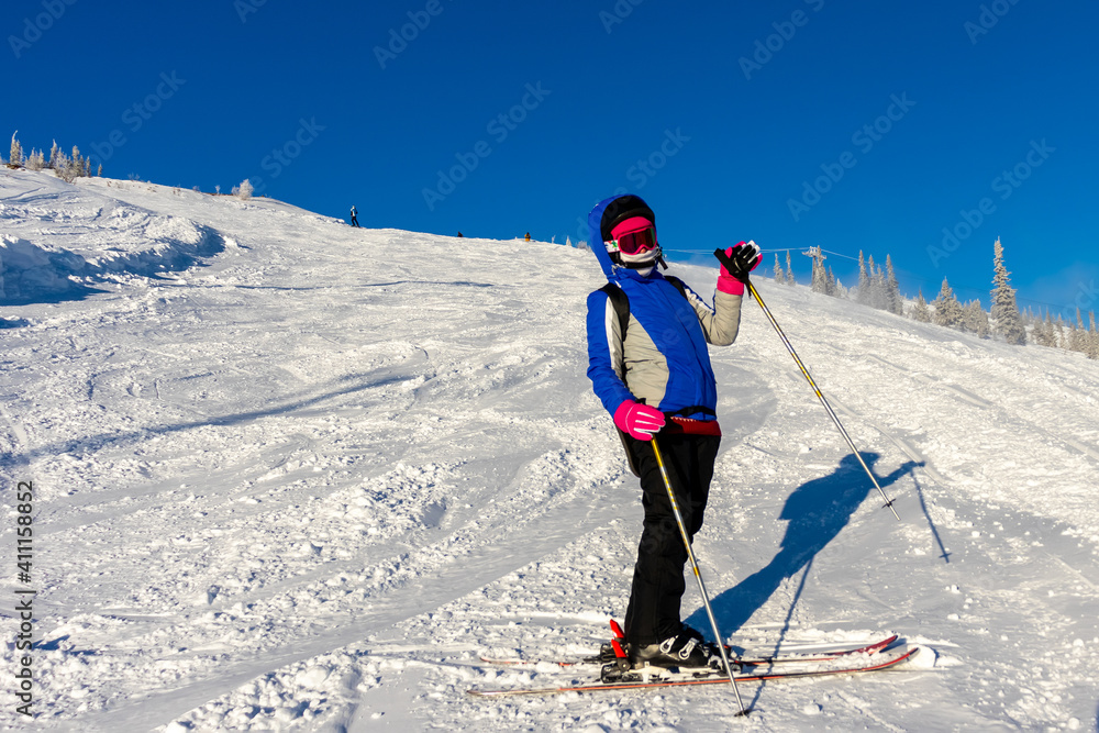 a girl skier stands on a ski slope and waves her hand on a sunny winter day