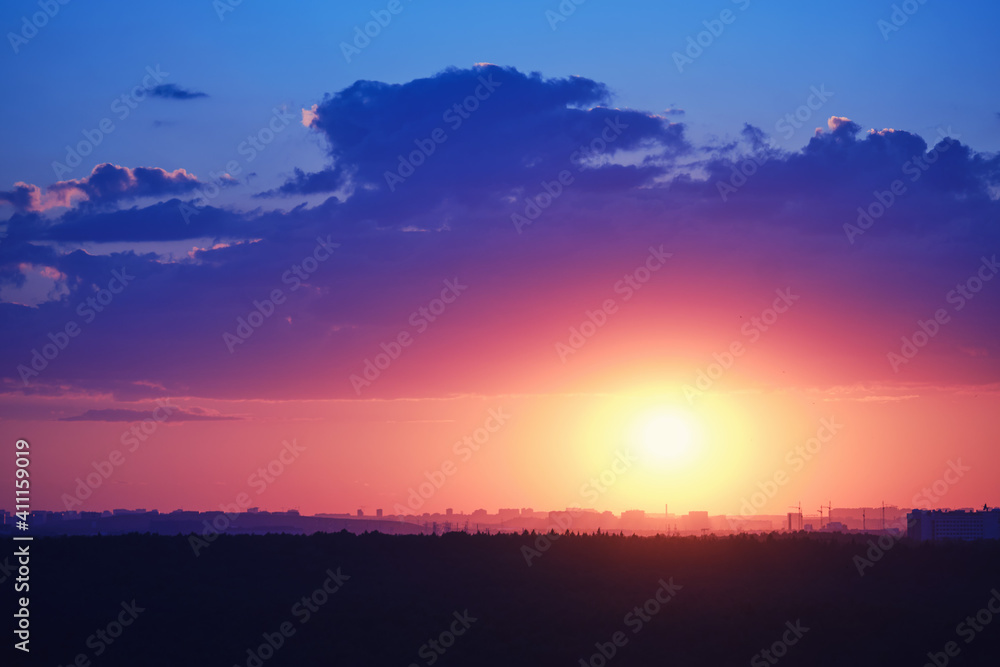 Fototapeta premium Beautiful setting red sun behind town houses and blue clouds