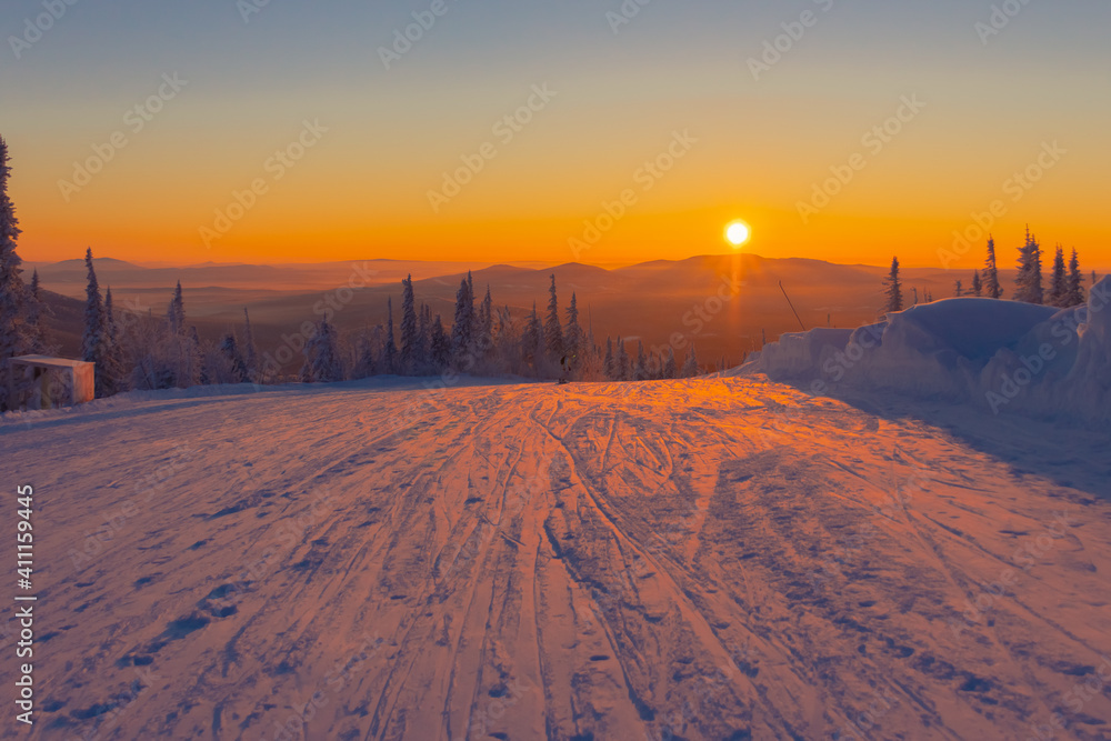 The setting sun illuminates the ski run in winter