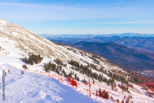 A ski track fenced with red mesh. Skiers and snowboarders descend on the slope