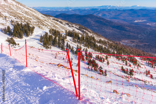 red grid fence on ski slope. steep Steep descent and beautiful landscape behind the fence photo