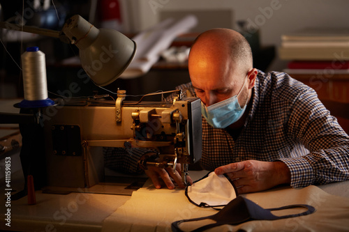 man working with sewing machine doing homemade face mask for preventing and stop corona virus spreading photo