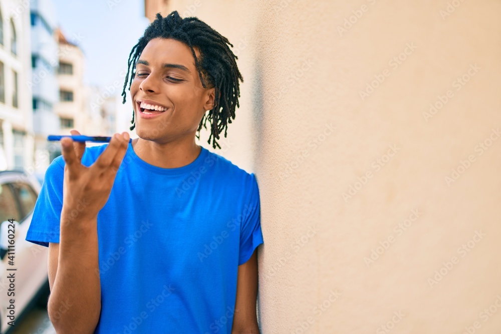 Young african american man sending audio message using smartphone at street of city. Young african american man sending audio message using smartphone at street of city.