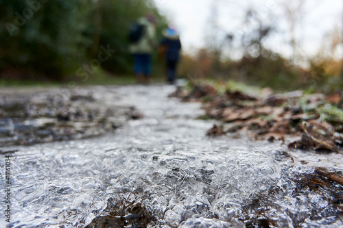 Zwei Menschen von hinten in einer Winterlandschaft mit auf dem Boden zu Eis gefrorenen Wasser im Vordergrund 