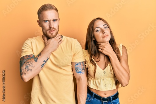 Young couple of girlfriend and boyfriend hugging and standing together touching painful neck, sore throat for flu, clod and infection