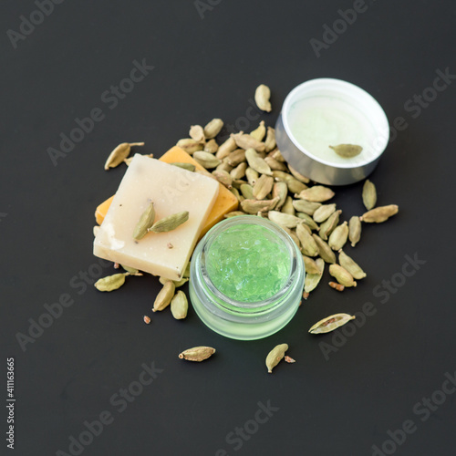 Two small bars of soap and a glass jar with cardamom-based cosmetic gel on a dark background with copy space. Selective focus.