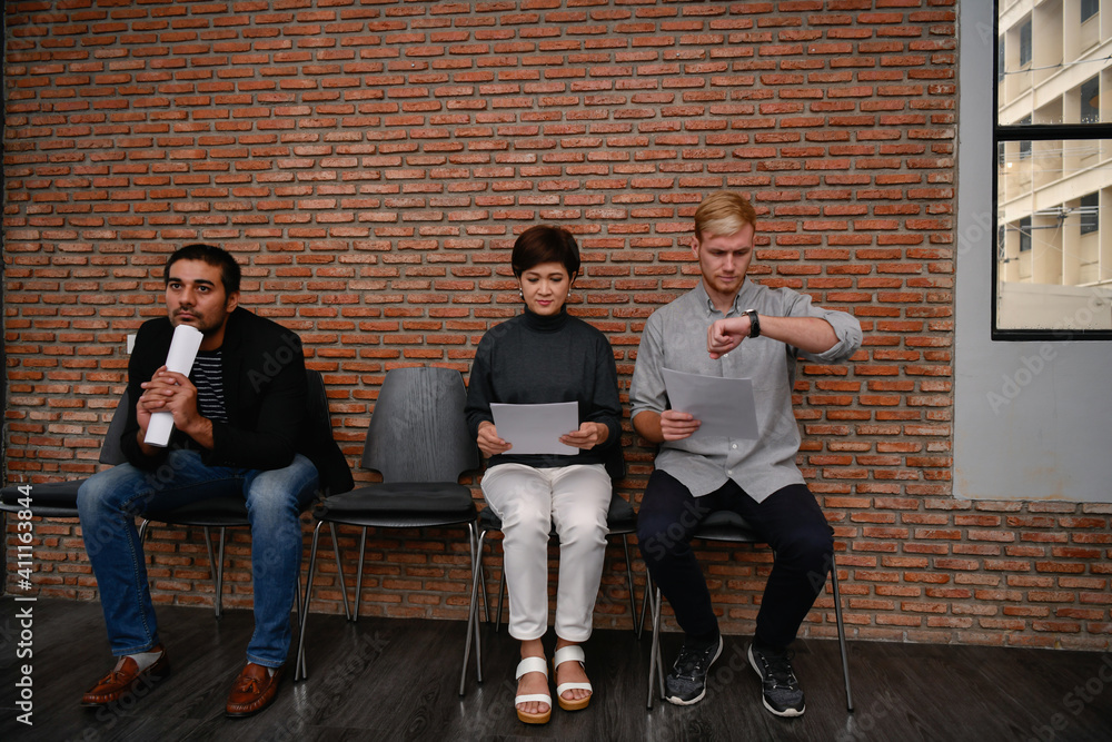 Full Length Of Business Colleagues Waiting While Sitting Against Brick Wall In Office - obrazy, fototapety, plakaty 