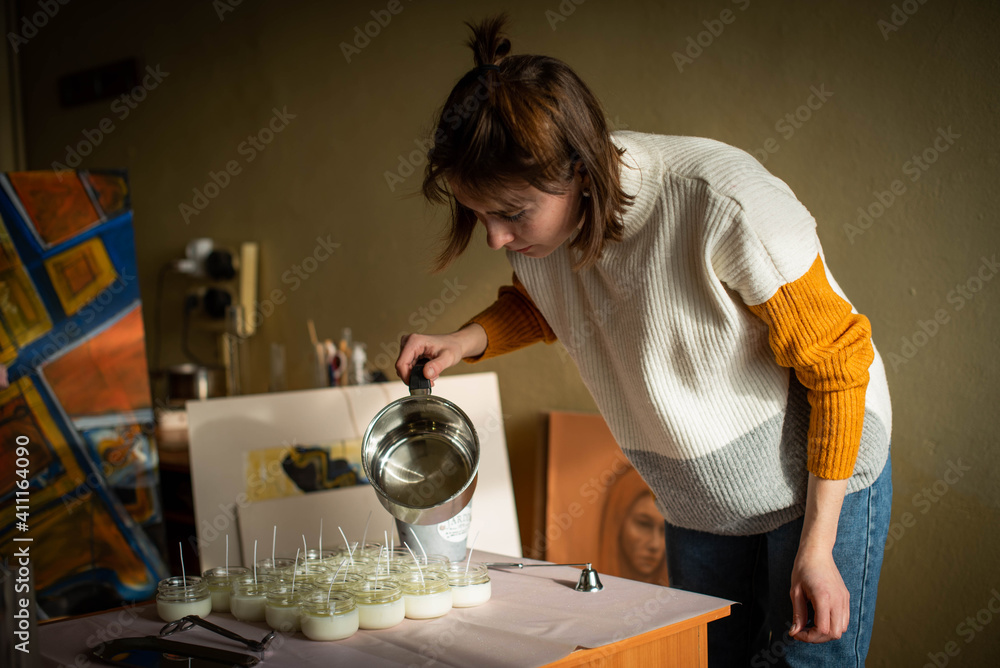Woman pouring melted wax into amber candles container. Ecological and vegan business. Soya wax candle accessories. Handmade with love. Remote work, online shop, workplace Woman pouring melted wax into amber candles container. Ecological and vegan business. Soya wax candle accessories. Handmade with love. Remote work, online shop, workplace