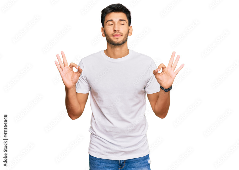 Young handsome man wearing casual white tshirt relax and smiling with eyes closed doing meditation gesture with fingers. yoga concept. Young handsome man wearing casual white tshirt relax and smiling with eyes closed doing meditation gesture with fingers. yoga concept.