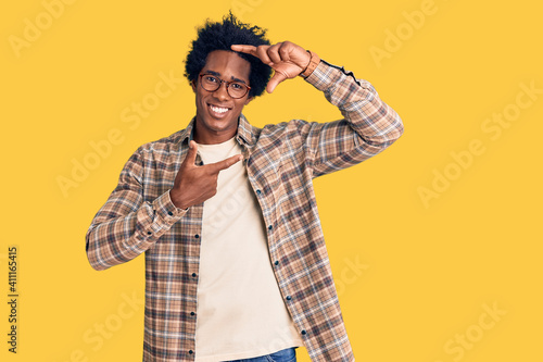 Handsome african american man with afro hair wearing casual clothes and glasses smiling making frame with hands and fingers with happy face. creativity and photography concept.