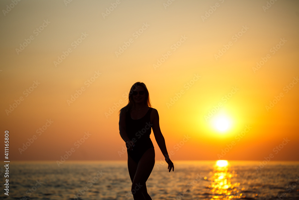 Silhouettes of a girl against the background of the sea and the setting sun