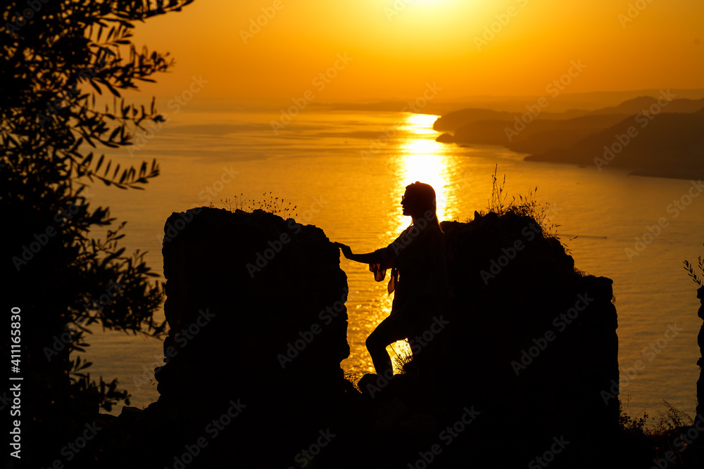 Silhouettes of a girl against the background of the sea and the setting sun