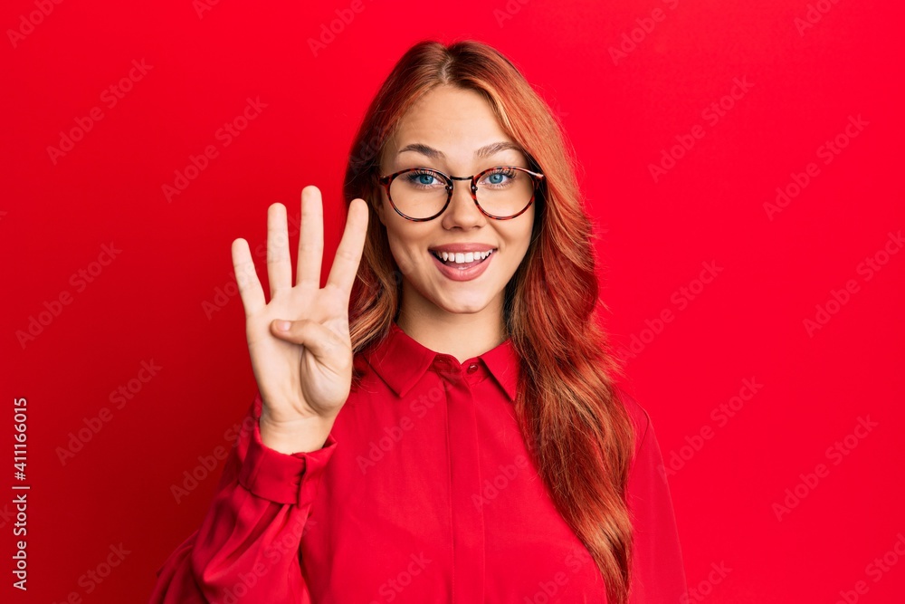 Young beautiful redhead woman wearing casual clothes and glasses over red background showing and pointing up with fingers number four while smiling confident and happy. Young beautiful redhead woman wearing casual clothes and glasses over red background showing and pointing up with fingers number four while smiling confident and happy.
