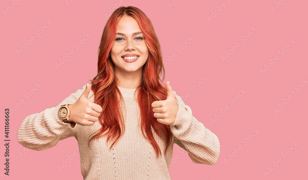 Young redhead woman wearing casual winter sweater success sign doing positive gesture with hand, thumbs up smiling and happy. cheerful expression and winner gesture. Young redhead woman wearing casual winter sweater success sign doing positive gesture with hand, thumbs up smiling and happy. cheerful expression and winner gesture.