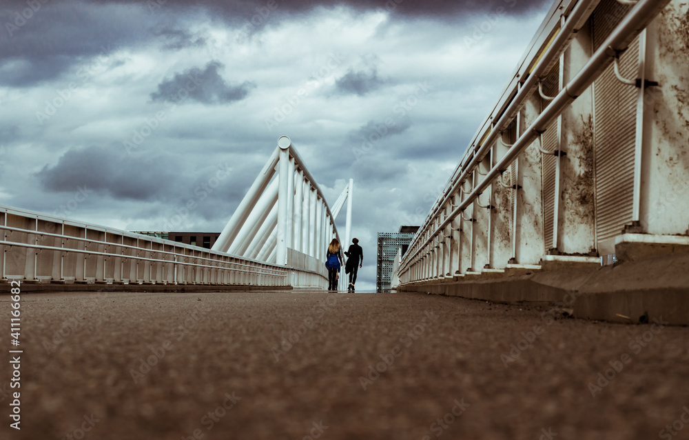 Fototapeta premium modern city architecture, footbridge under cloudy sky, with people silhouettes