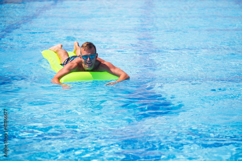 Handsome young man swims on inflatable mattress in blue pool
