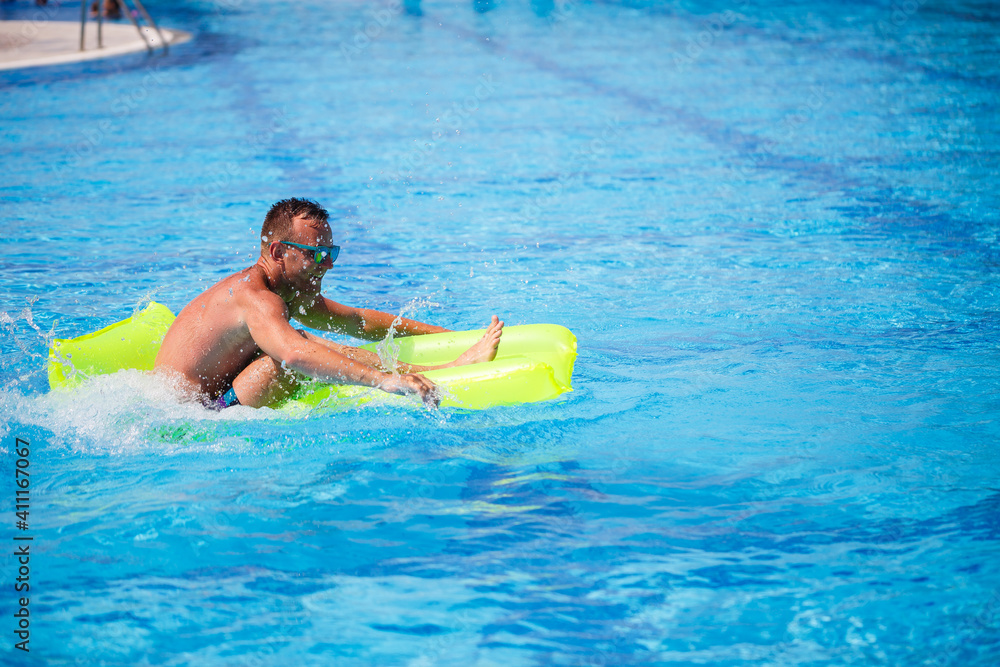 Handsome young man swims on inflatable mattress in blue pool