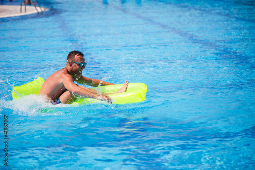 Handsome young man swims on inflatable mattress in blue pool