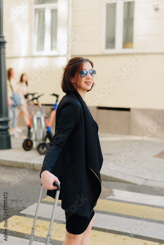 Beautiful woman in black dress on a background of an urban landscape with a suitcase © ShevarevAlex