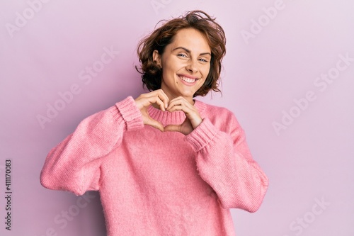 Young brunette woman wearing casual winter sweater smiling in love doing heart symbol shape with hands. romantic concept.