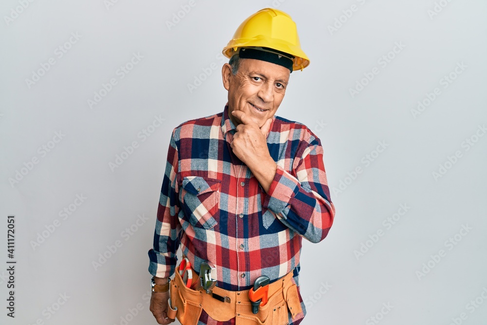 Senior hispanic man wearing handyman uniform looking confident at the camera smiling with crossed arms and hand raised on chin. thinking positive. Senior hispanic man wearing handyman uniform looking confident at the camera smiling with crossed arms and hand raised on chin. thinking positive.