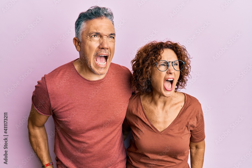 Beautiful middle age couple together wearing casual clothes angry and mad screaming frustrated and furious, shouting with anger. rage and aggressive concept. Beautiful middle age couple together wearing casual clothes angry and mad screaming frustrated and furious, shouting with anger. rage and aggressive concept.