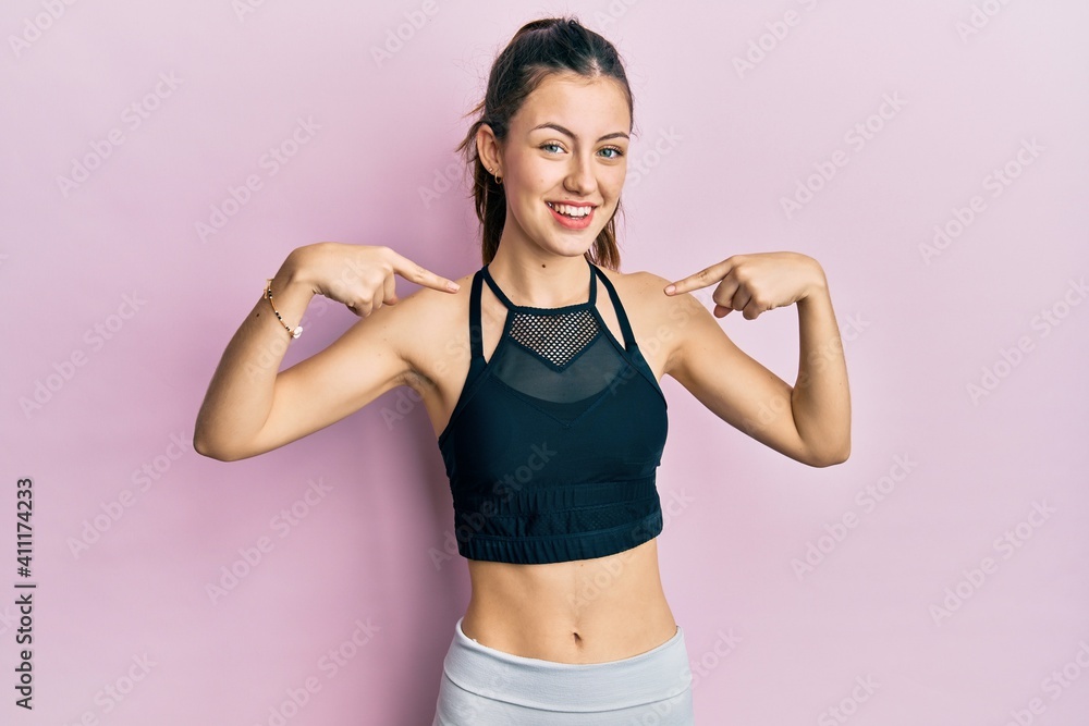 Young brunette woman wearing sportswear looking confident with smile on face, pointing oneself with fingers proud and happy.