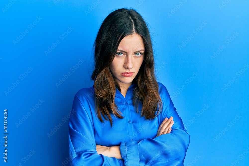 Young brunette woman wearing casual blue shirt skeptic and nervous, disapproving expression on face with crossed arms. negative person. Young brunette woman wearing casual blue shirt skeptic and nervous, disapproving expression on face with crossed arms. negative person.