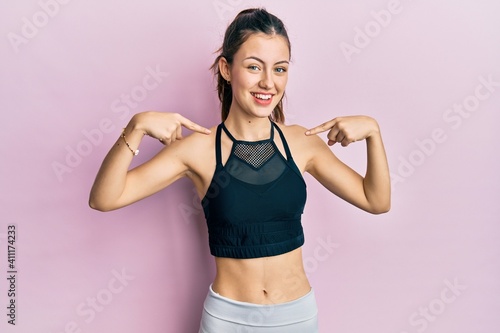 Young brunette woman wearing sportswear looking confident with smile on face  pointing oneself with fingers proud and happy.
