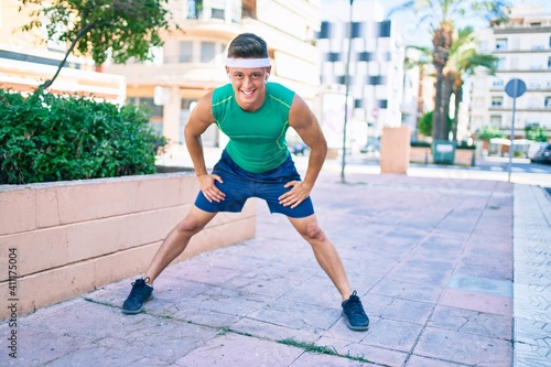 Young hispanic sportsman using earphones stretching at street of city