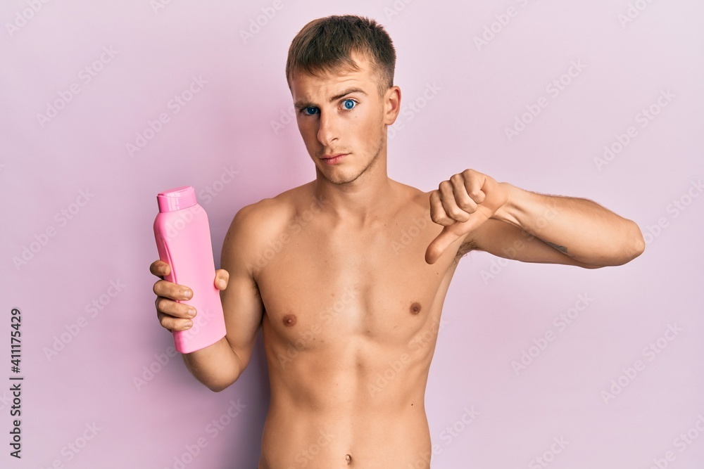 Young caucasian man shirtless holding shampoo bottle with angry face, negative sign showing dislike with thumbs down, rejection concept Young caucasian man shirtless holding shampoo bottle with angry face, negative sign showing dislike with thumbs down, rejection concept