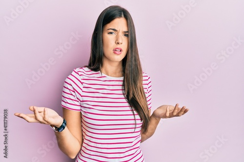 Young brunette woman wearing casual clothes over pink background clueless and confused with open arms, no idea concept. © Krakenimages.com