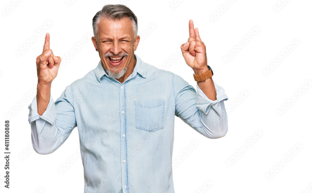 Middle age grey-haired man wearing casual clothes shouting with crazy expression doing rock symbol with hands up. music star. heavy music concept. Middle age grey-haired man wearing casual clothes shouting with crazy expression doing rock symbol with hands up. music star. heavy music concept.