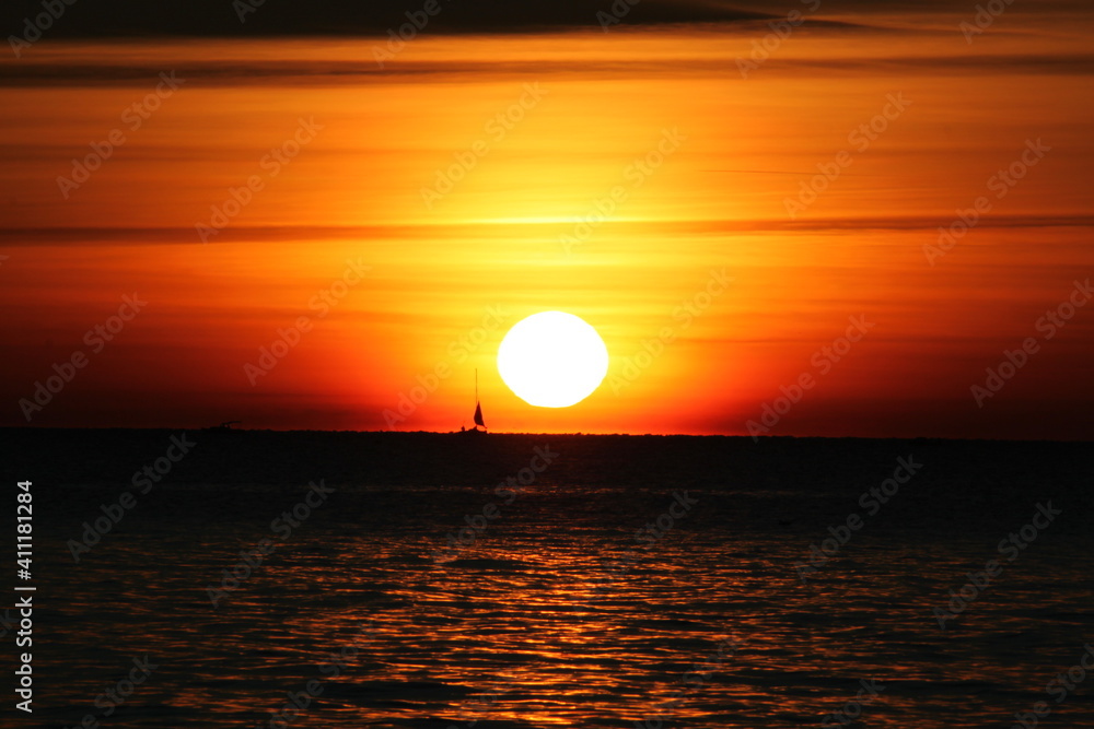 Große Sonne kurz vor Sonnenuntergang mit Segelschiff am Horizont links