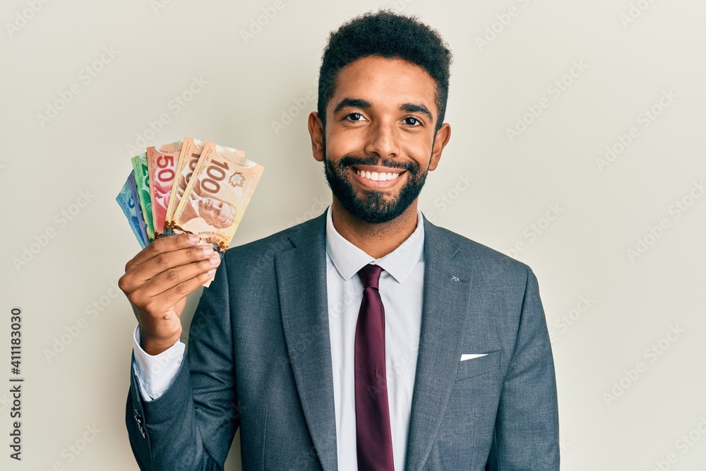 Handsome hispanic business man with beard holding canadian dollars looking positive and happy standing and smiling with a confident smile showing teeth