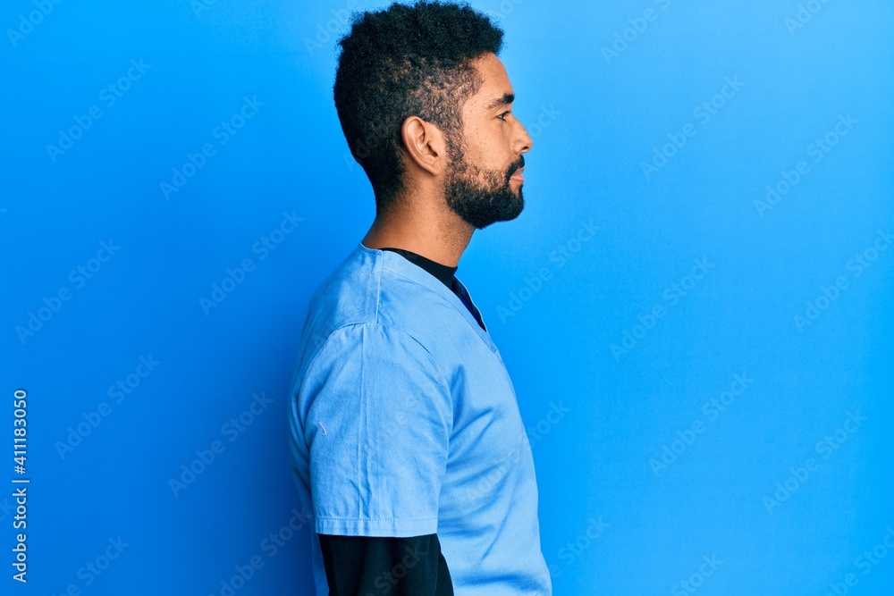 Handsome hispanic man with beard wearing blue male nurse uniform looking to side, relax profile pose with natural face with confident smile. Handsome hispanic man with beard wearing blue male nurse uniform looking to side, relax profile pose with natural face with confident smile.