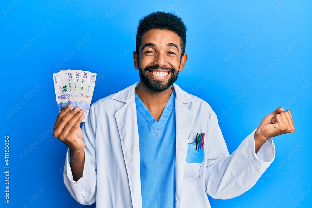 Handsome hispanic man with beard wearing doctor uniform holding 50 colombian pesos screaming proud, celebrating victory and success very excited with raised arm Handsome hispanic man with beard wearing doctor uniform holding 50 colombian pesos screaming proud, celebrating victory and success very excited with raised arm