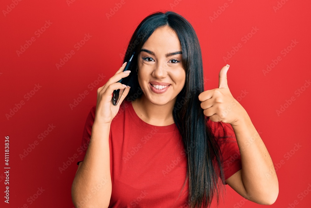 Young beautiful hispanic girl having conversation talking on the smartphone smiling happy and positive, thumb up doing excellent and approval sign Young beautiful hispanic girl having conversation talking on the smartphone smiling happy and positive, thumb up doing excellent and approval sign