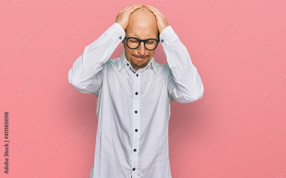 Bald man with beard wearing business shirt and glasses suffering from headache desperate and stressed because pain and migraine. hands on head. Bald man with beard wearing business shirt and glasses suffering from headache desperate and stressed because pain and migraine. hands on head.
