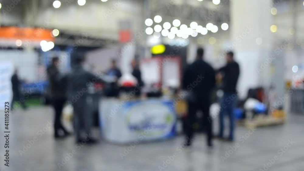 Blurred background. People walk inside large space building. Exhibition presentation. Abstract background and bokeh spots with moving people indoors. Hall, lobby, entry. People walk inside space. Blurred background. People walk inside large space building. Exhibition presentation. Abstract background and bokeh spots with moving people indoors. Hall, lobby, entry. People walk inside space.