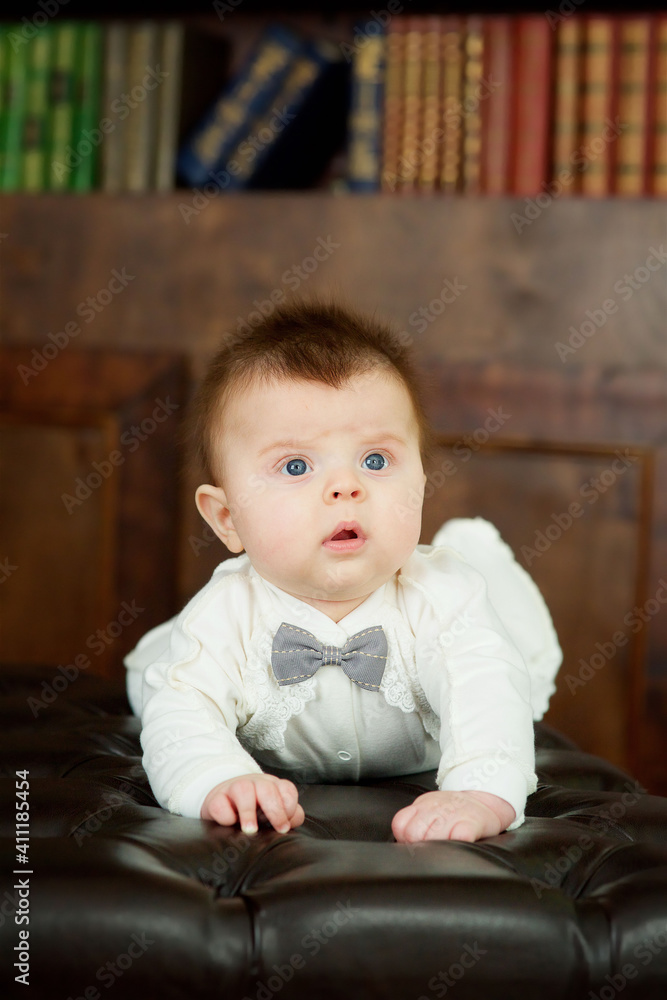 A baby boy is lying on a soft surface. In the background is a library with books. A baby boy is lying on a soft surface. In the background is a library with books.