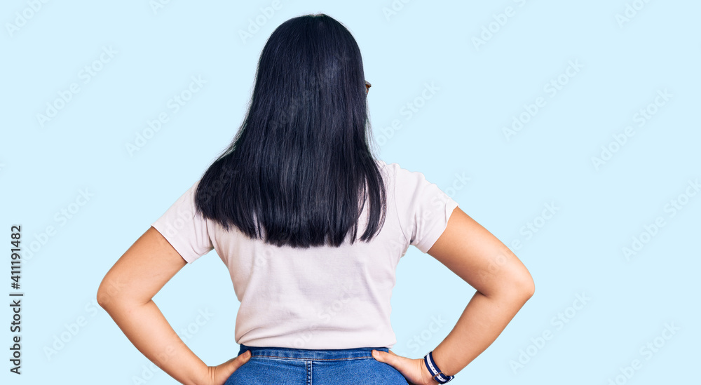 Young beautiful asian girl wearing casual clothes and glasses standing backwards looking away with arms on body Young beautiful asian girl wearing casual clothes and glasses standing backwards looking away with arms on body