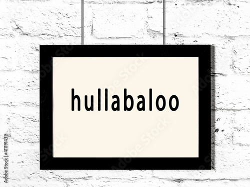 Black frame hanging on white brick wall with inscription hullabaloo photo