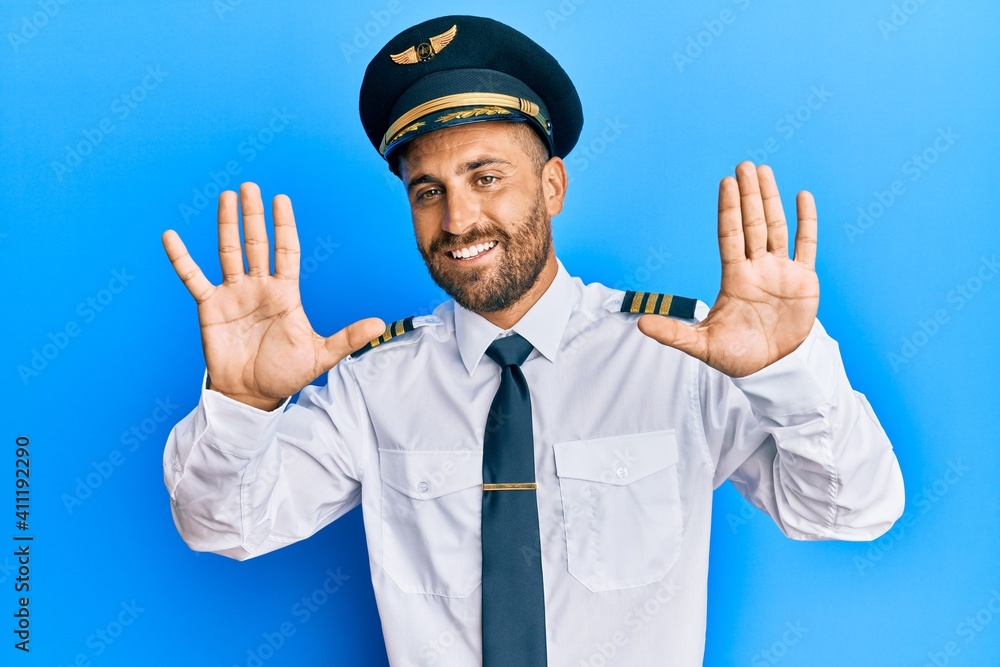 Handsome man with beard wearing airplane pilot uniform showing and pointing up with fingers number ten while smiling confident and happy. Handsome man with beard wearing airplane pilot uniform showing and pointing up with fingers number ten while smiling confident and happy.