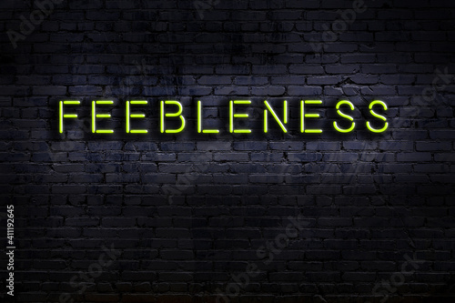Neon sign. Word feebleness against brick wall. Night view
