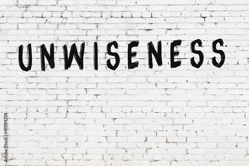 Bild auf Leinwand White wall with black paint inscription unwiseness on it